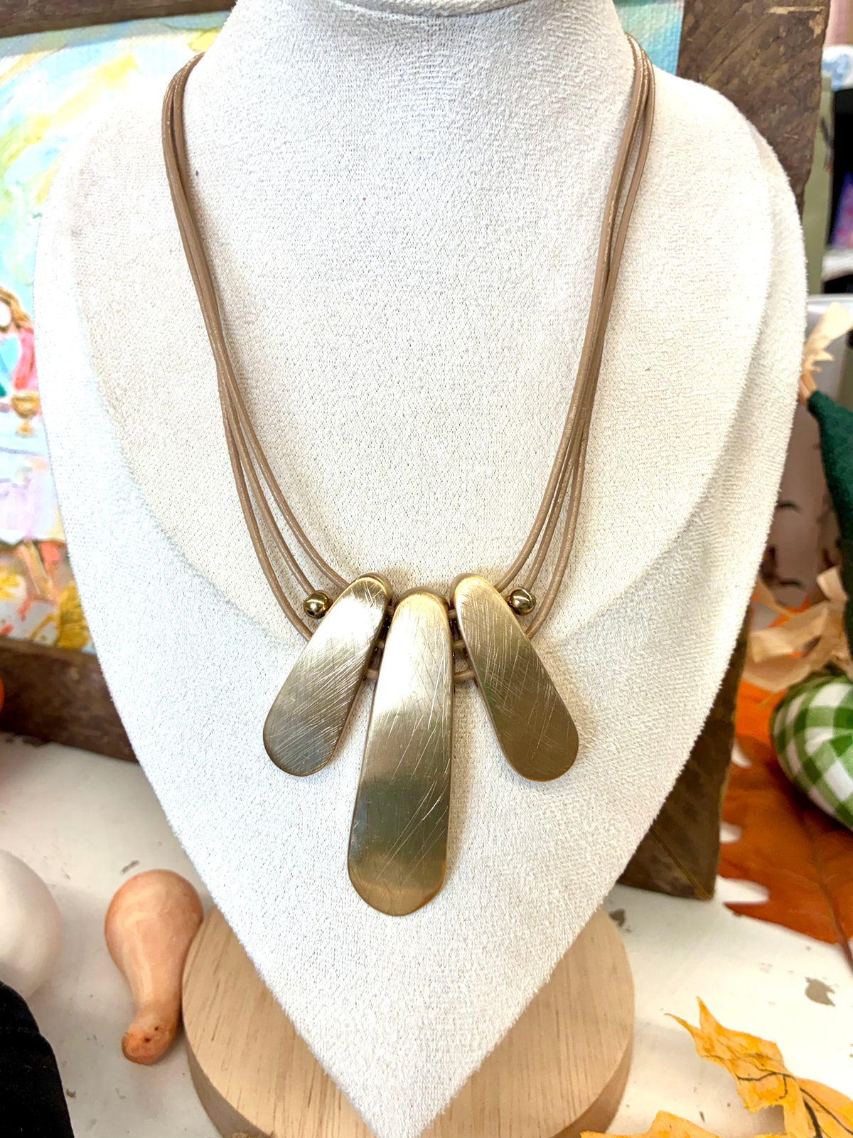 Multi-strand leather cord statement necklace featuring three textured, teardrop-shaped brass pendant plates hanging in the center