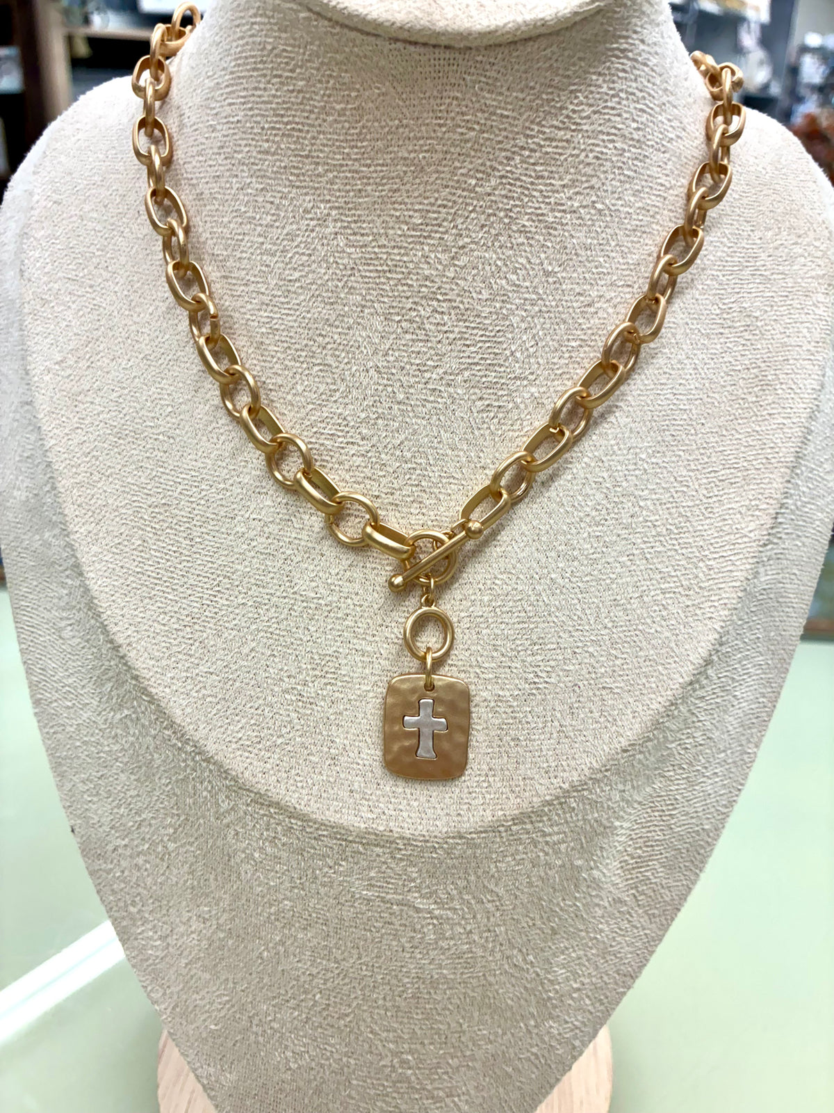 Gold-tone chunky chain toggle necklace featuring a hammered square pendant with a small cross detail.