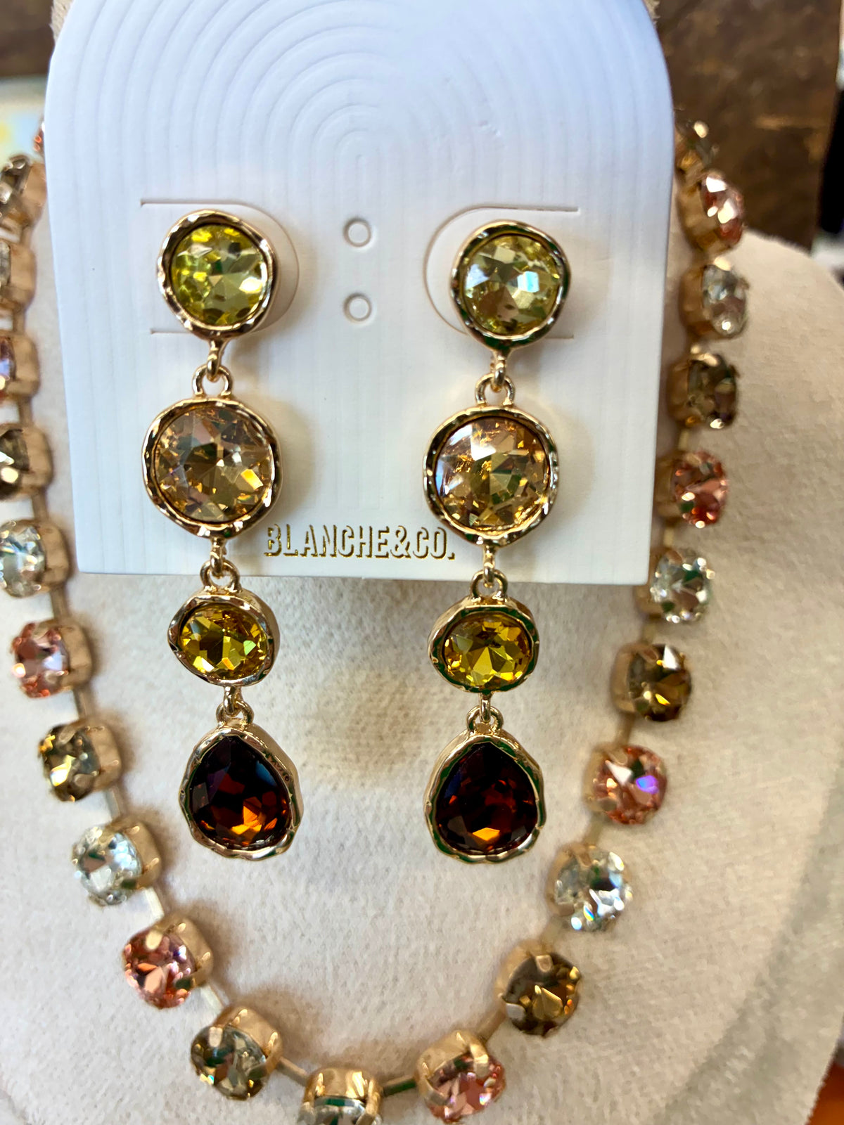 Multi-stone crystal collar necklace featuring faceted round stones in alternating metallic, rose, and smoky tones / Gold-tone linear drop earrings featuring a cascading gradient of sparkling yellow, olive, and amber-toned crystal stone.