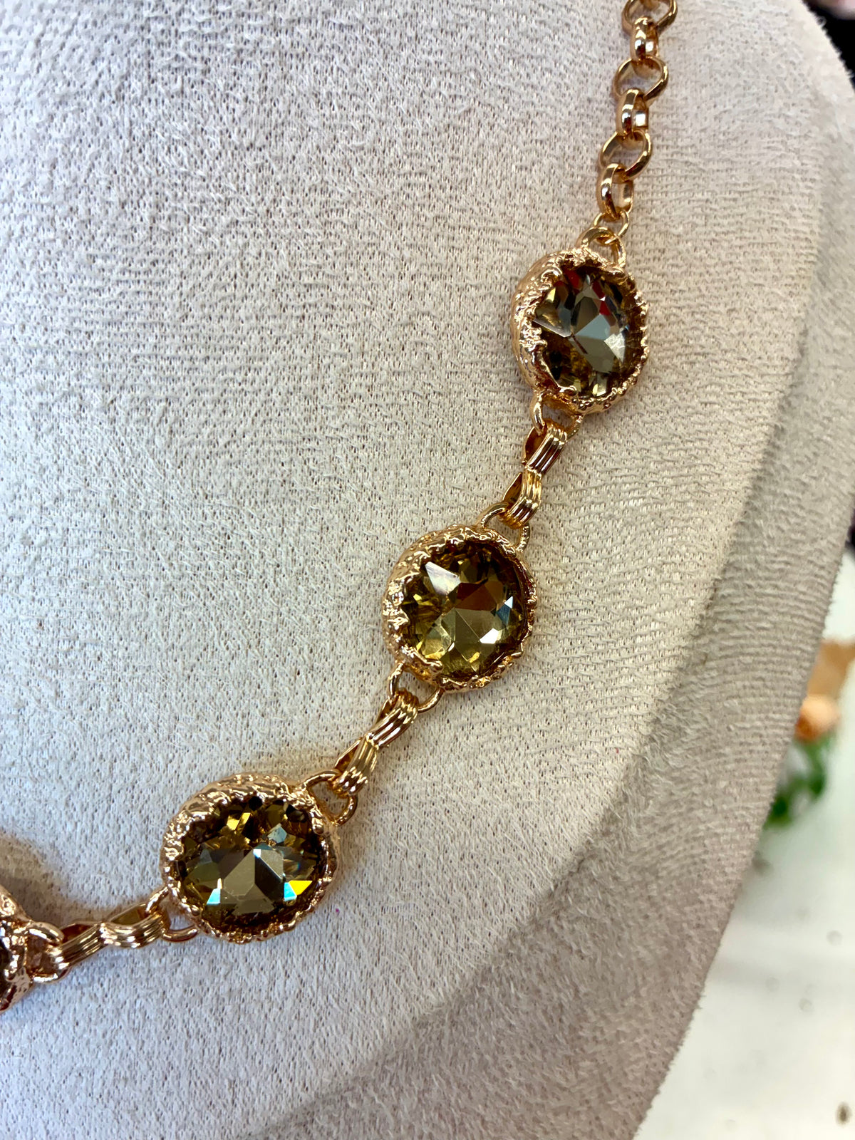 Gold tone link necklace featuring faceted olive-green round crystal stations in prong settings.