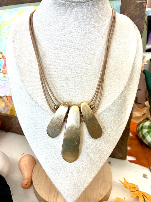 Multi-strand leather cord statement necklace featuring three textured, teardrop-shaped brass pendant plates hanging in the center