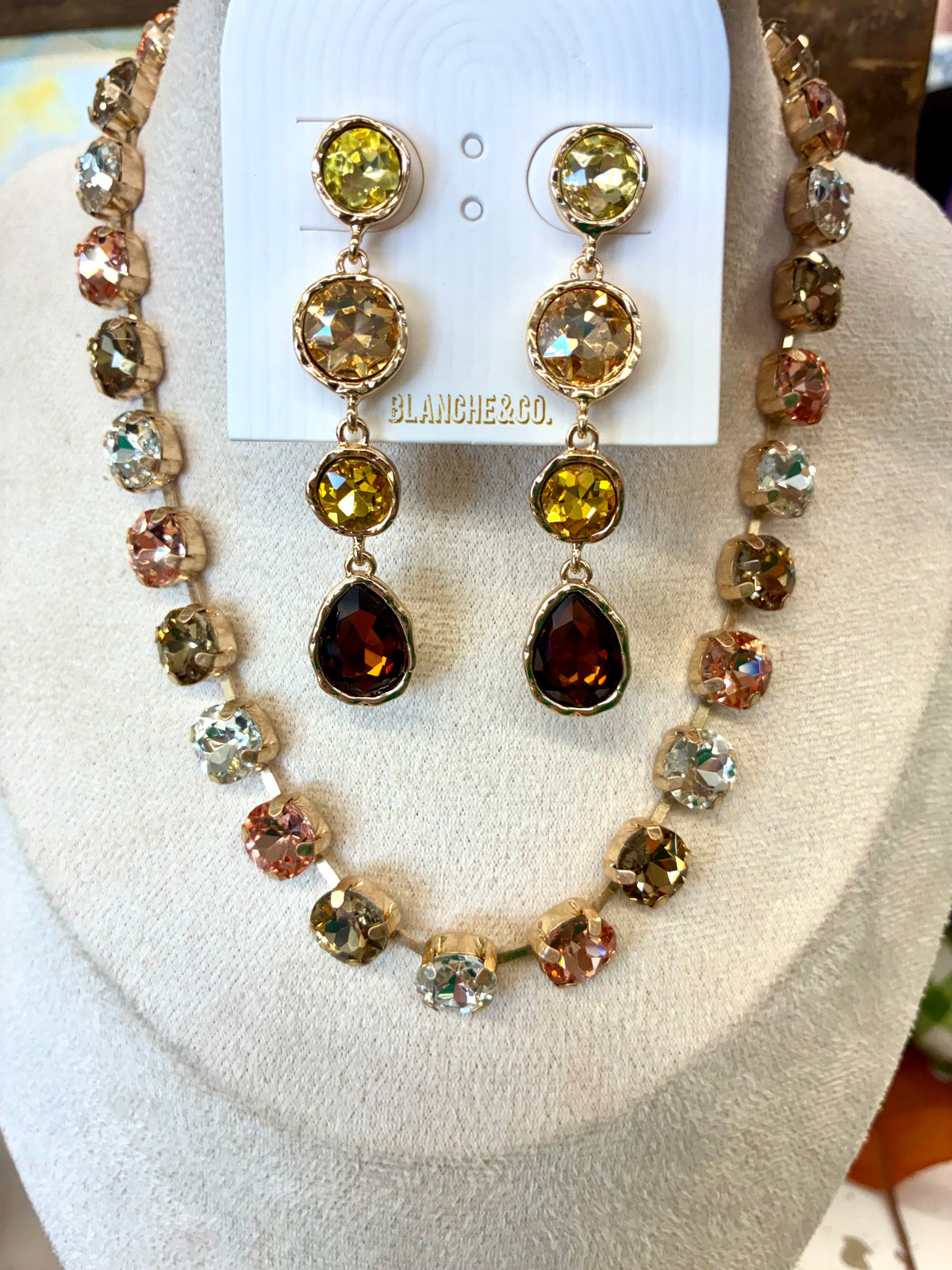 Multi-stone crystal collar necklace featuring faceted round stones in alternating metallic, rose, and smoky tones / Gold-tone linear drop earrings featuring a cascading gradient of sparkling yellow, olive, and amber-toned crystal stone.