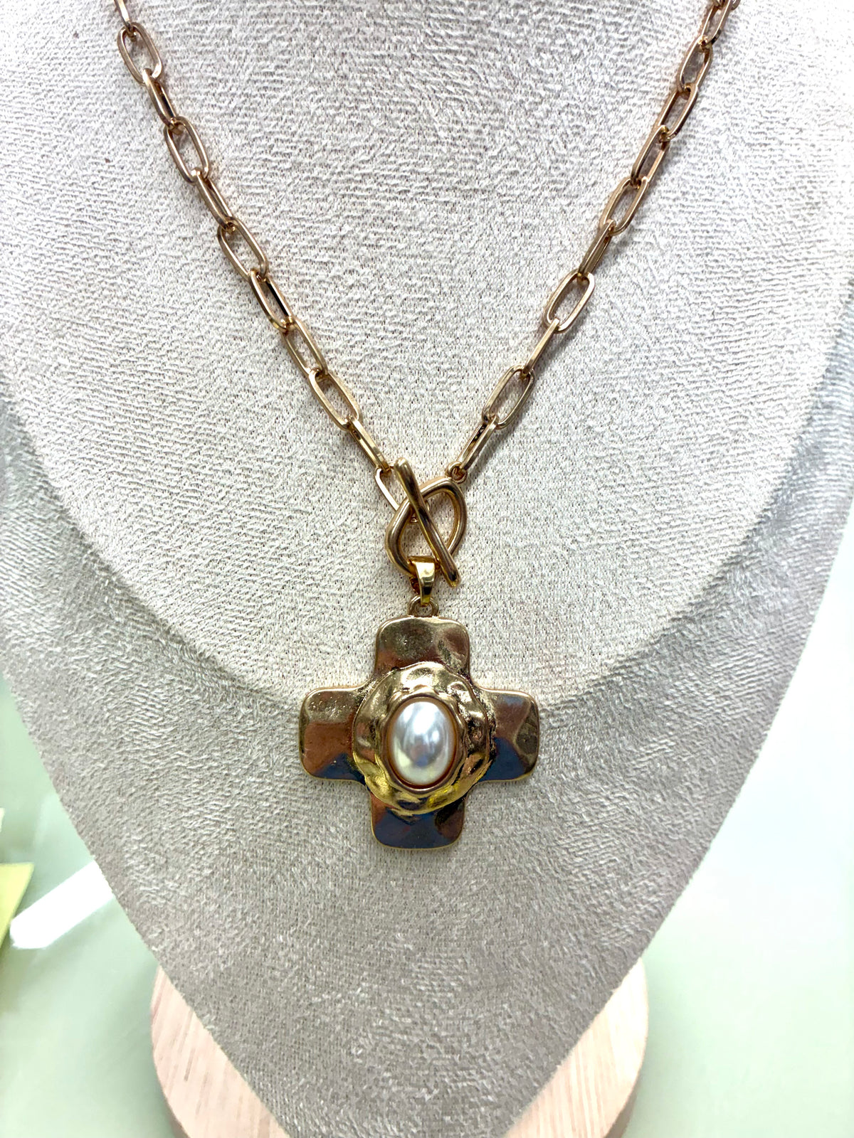 Gold-tone hammered cross necklace and matching earrings sold separately set featuring a central pearl accent and a toggle clasp.