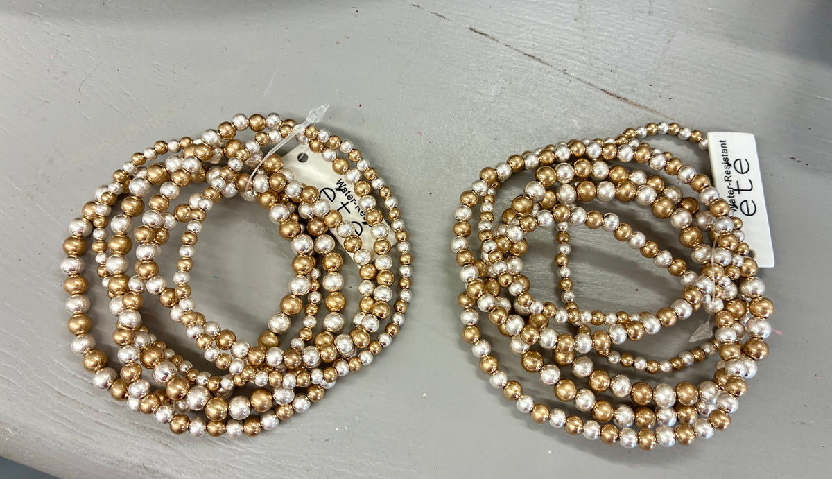 Six-strand mixed-metal beaded stretch bracelet stack featuring alternating silver and gold-toned metallic beads of varying sizes. WATER RESISTANT