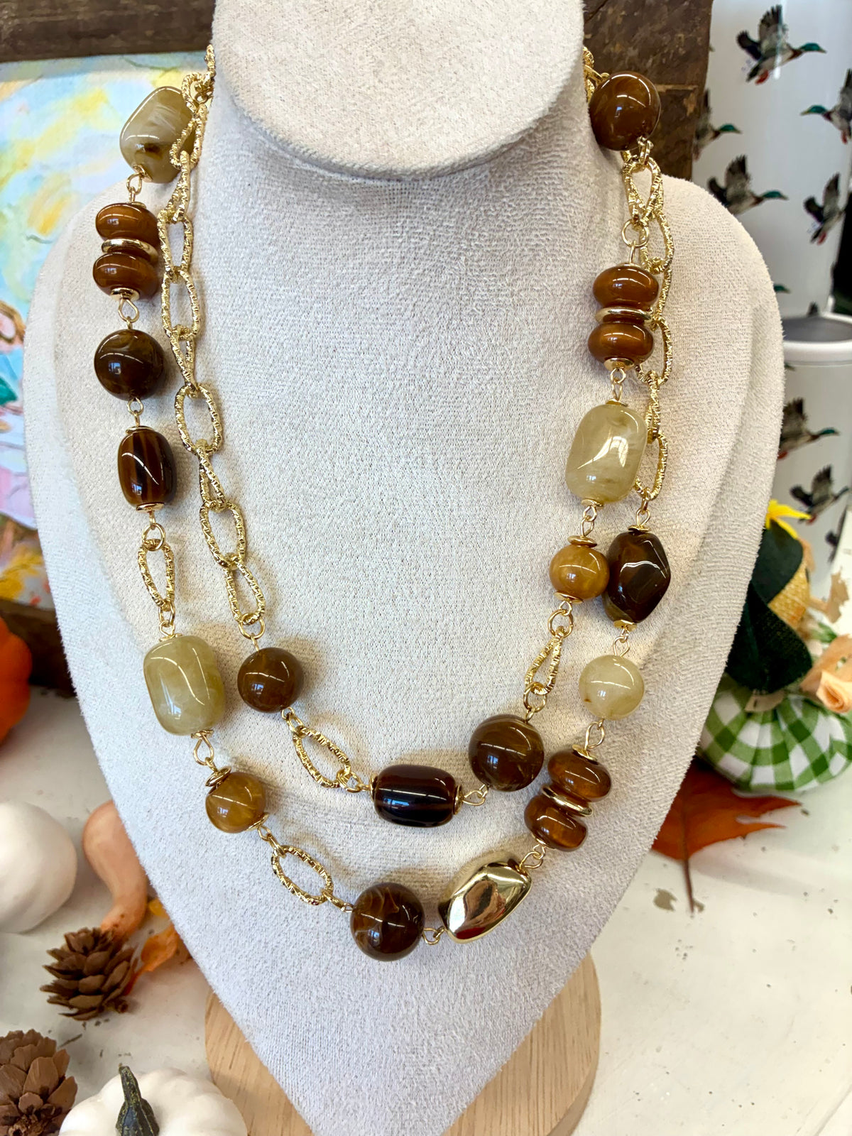 Multi-strand gold-tone chain necklace featuring polished caramel, amber-colored, and beige natural or resin beads.