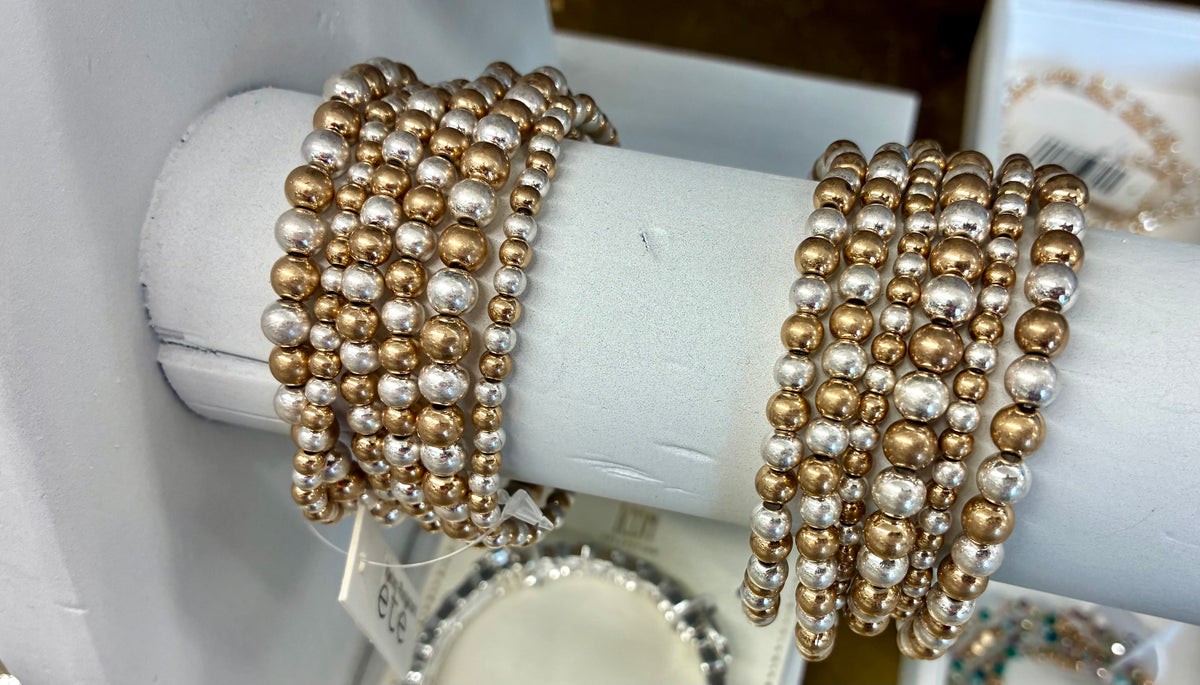 Six-strand mixed-metal beaded stretch bracelet stack featuring alternating silver and gold-toned metallic beads of varying sizes. WATER RESISTANT