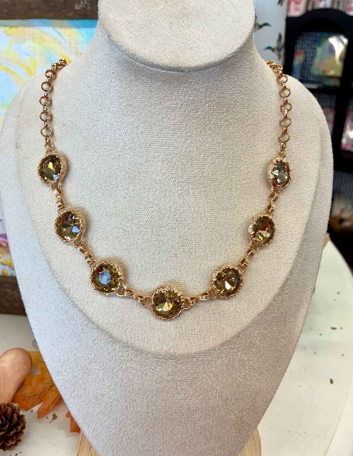 Gold tone link necklace featuring faceted olive-green round crystal stations in prong settings.